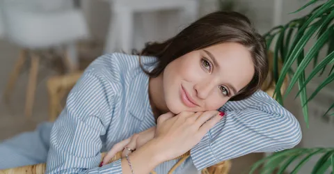 izobrazenie-krasivoi-molodoi-zensiny-modeli-s-temnymi-volosami-sidasei-na-derevannom-stule-imeet-rasslablennoe-vyrazenie-lica-ocarovatel-nuu-ulybku-naslazdaetsa-domasnei-spokoinoi-atmosferoi-koncepcia-krasoty-i-emo