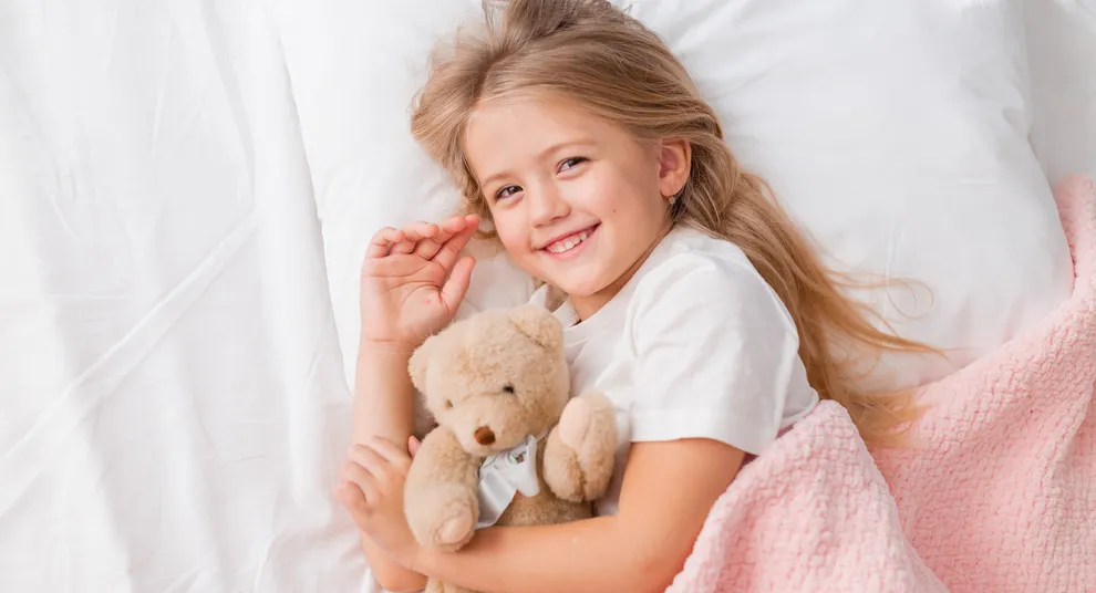 portrait-little-blonde-girl-lying-bed-with-teddy-bear-pink-blanket-top-view